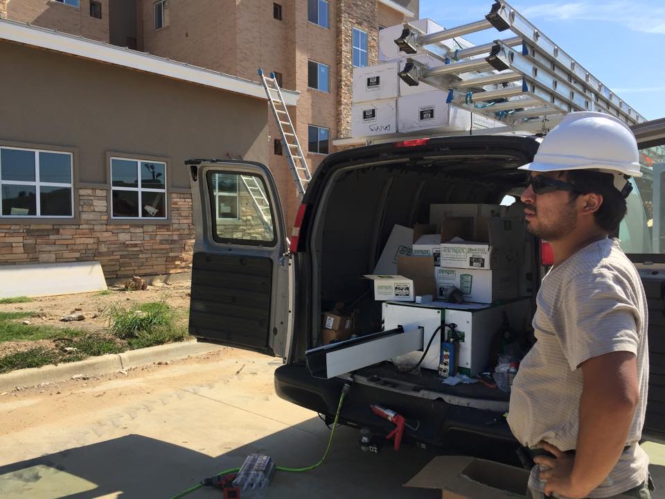Rain gutters installation - on this picture you can see a gutter making machine inside a cargo van ready to produce gutters in front of the commercial building. a gutter installer wearing a construction hard hat. rain gutter contractor, gutter company