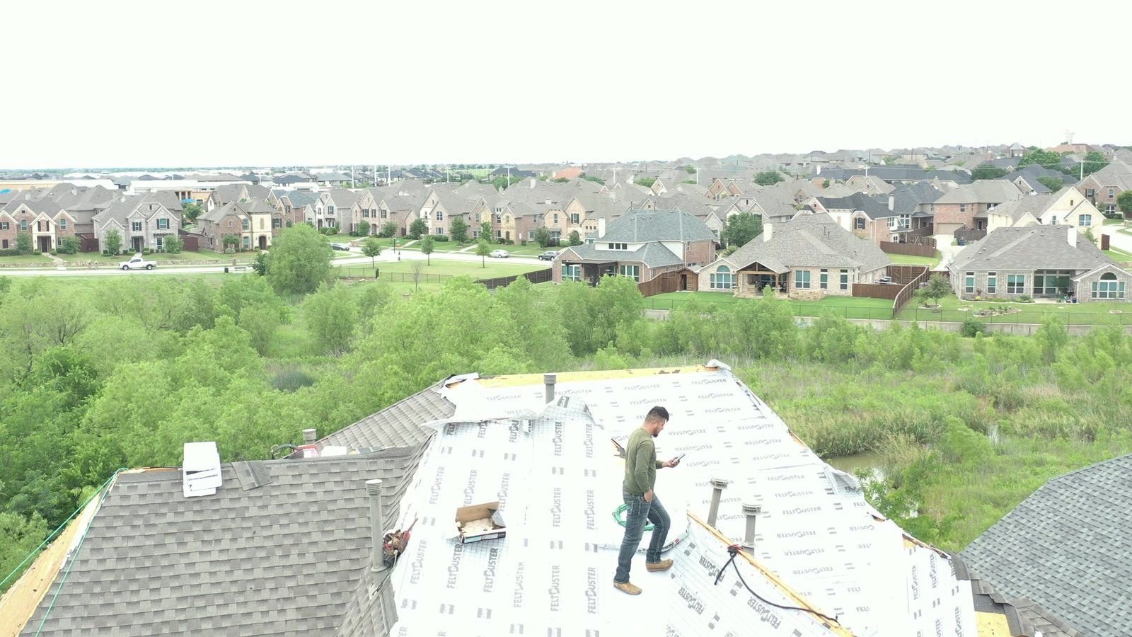 Drone view of a Roofing Giant crew installing a new roof on a Dallas–Fort Worth home, with the neighborhood in the background